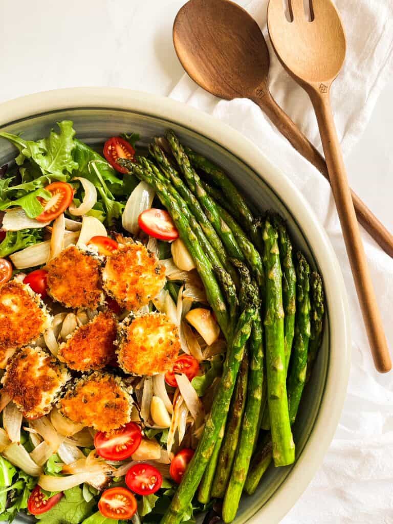 Assembled Asparagus Salad with Fried Goat Cheese containing sautéed asparagus, roasted onions & garlic, cherry tomatoes, greens and fried goat cheese