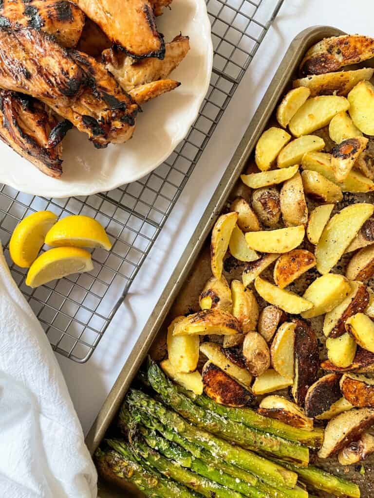 Photo of completed Oven Roasted Potatoes & Asparagus with Grilled Chicken.  Displayed on a plate and on a sheet pan.  Lemons for garnish.