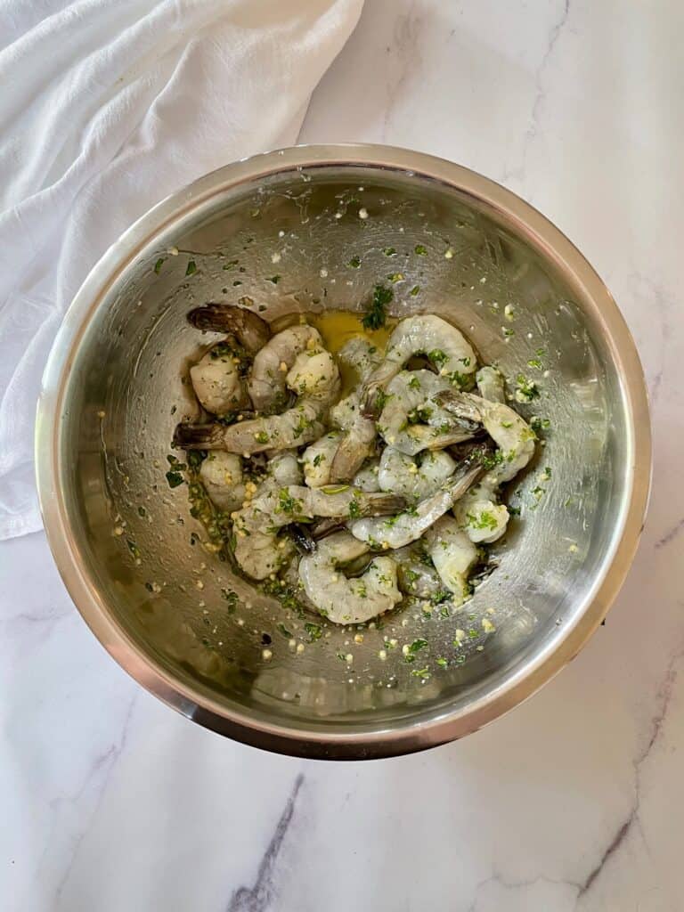 Shrimp in a medium sized mixing bowl soaking in the marinade.