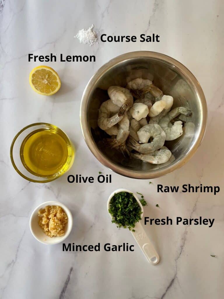 Ingredients needed for the shrimp marinade. Ingredients needed are raw shrimp, course salt, fresh lemon, olive oil, fresh parsley and minced garlic.