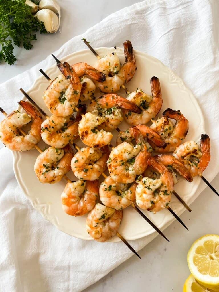 Fully cooked shrimp on skewers on a white plate with lemon and parsley. 