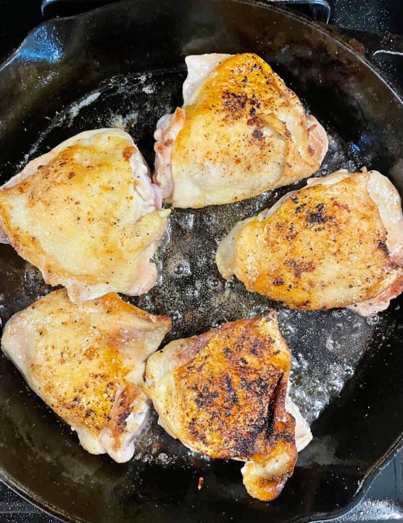 Chicken thighs in the cast iron skillet, flipped after the skin has finished searing. The skin is now golden brown. 