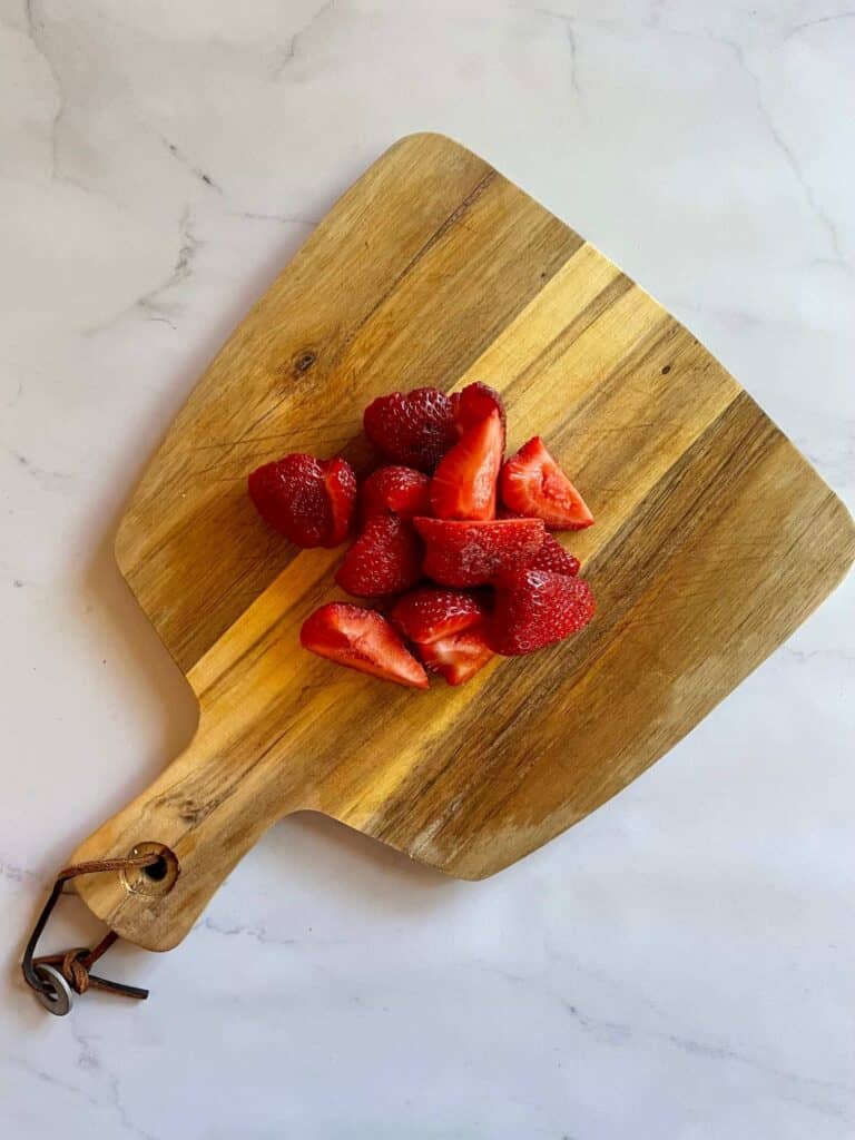 Strawberries chopped into large chunks on a cutting board. 
