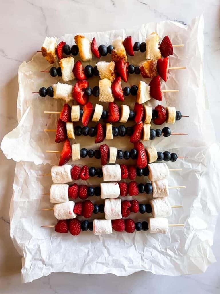 Fruit on skewers in all different combinations. Skewers are on parchment paper. 