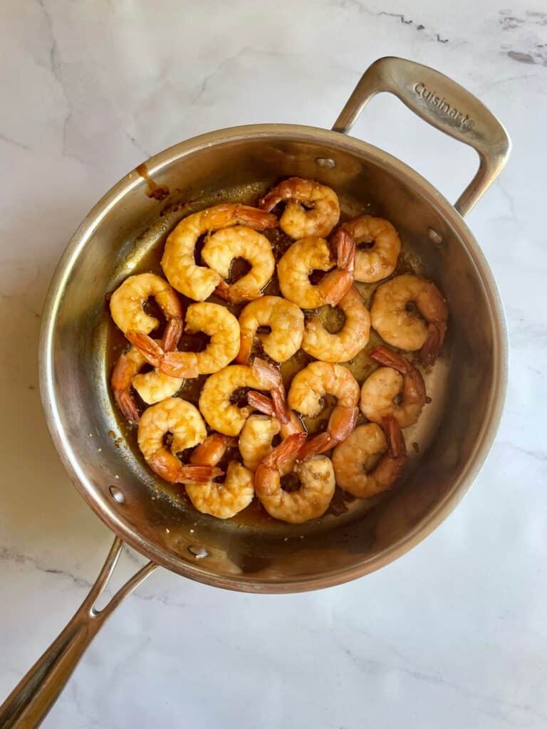 Teriyaki shrimp for the shrimp sushi bowl is cooked in a large frying pan.