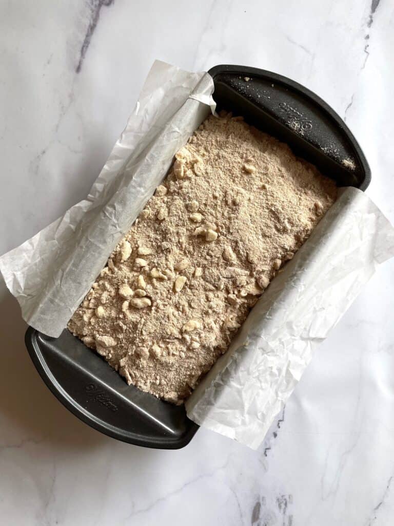 Banana bread batter in a parchment lined loaf pan. The batter is now topped with streusel. 