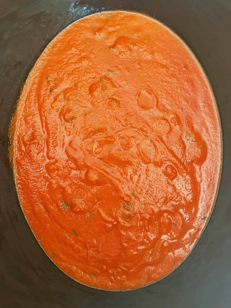 marinara sauce in the bottom of a slow cooker.