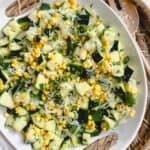 Sauteed zucchini and onion with sweet corn displayed in a white serving bowl on top of a brown basket.