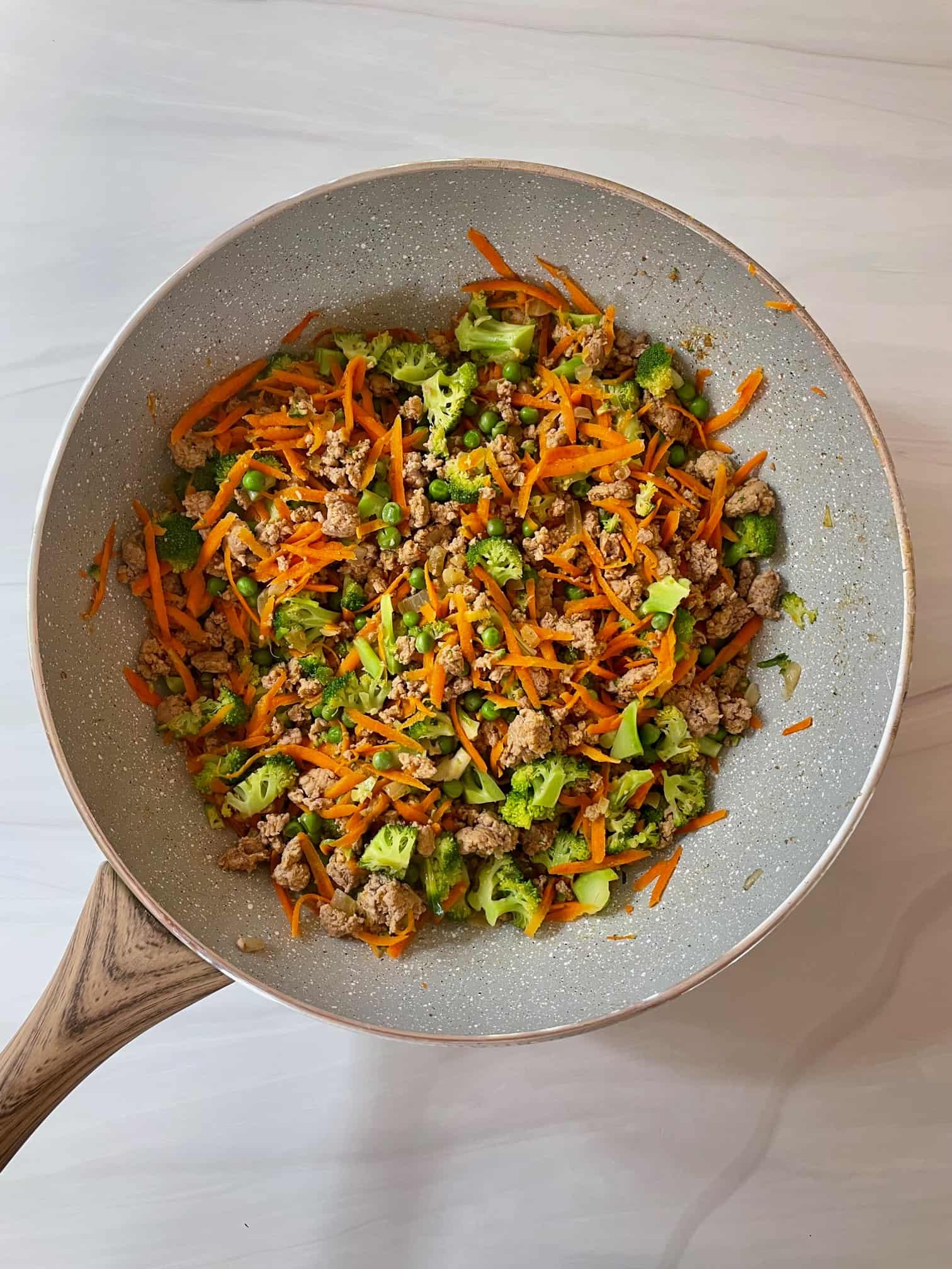 Ground turkey, shredded carrots, chopped broccoli, peas, onions and garlic in a large frying pan.