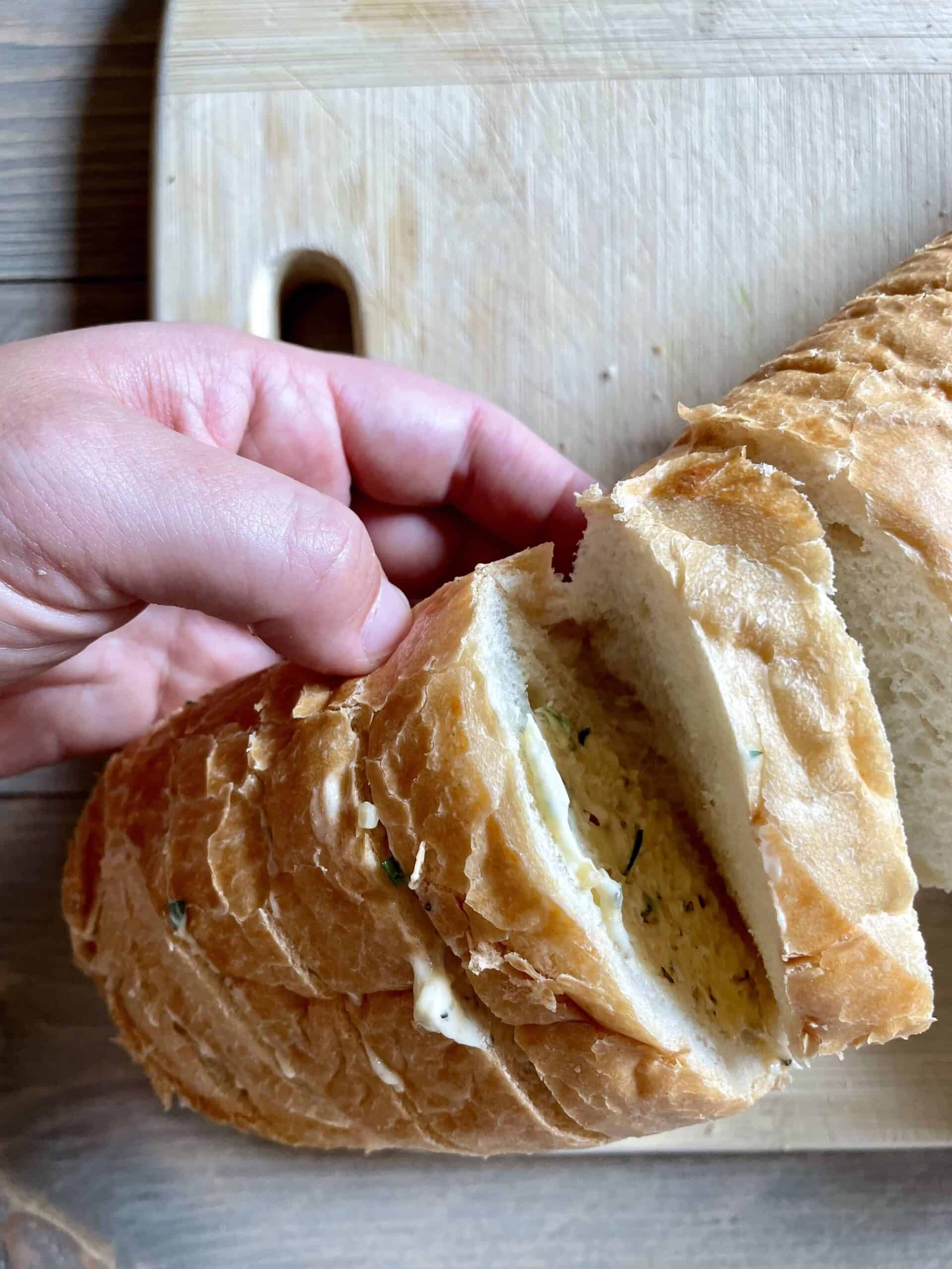 French bread slices are slathered with vegan garlic butter. The bread is held up with a hand.