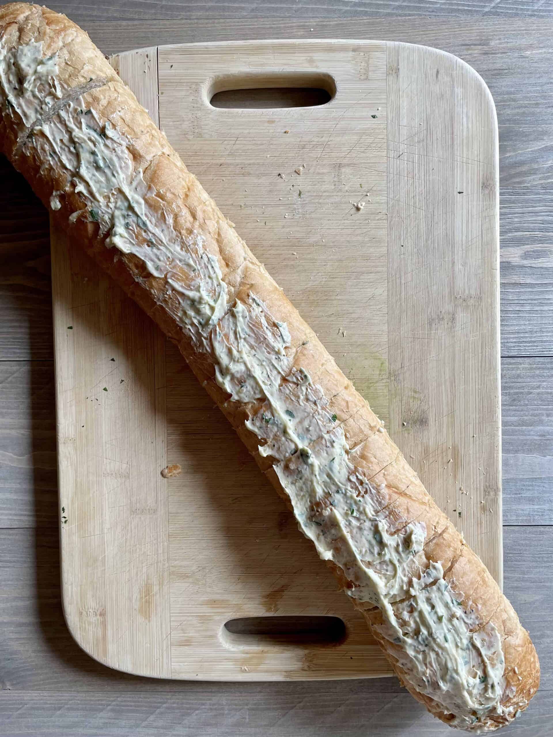 The loaf of vegan garlic bread is slathered with vegan garlic butter and laid out on a wooden cutting board.