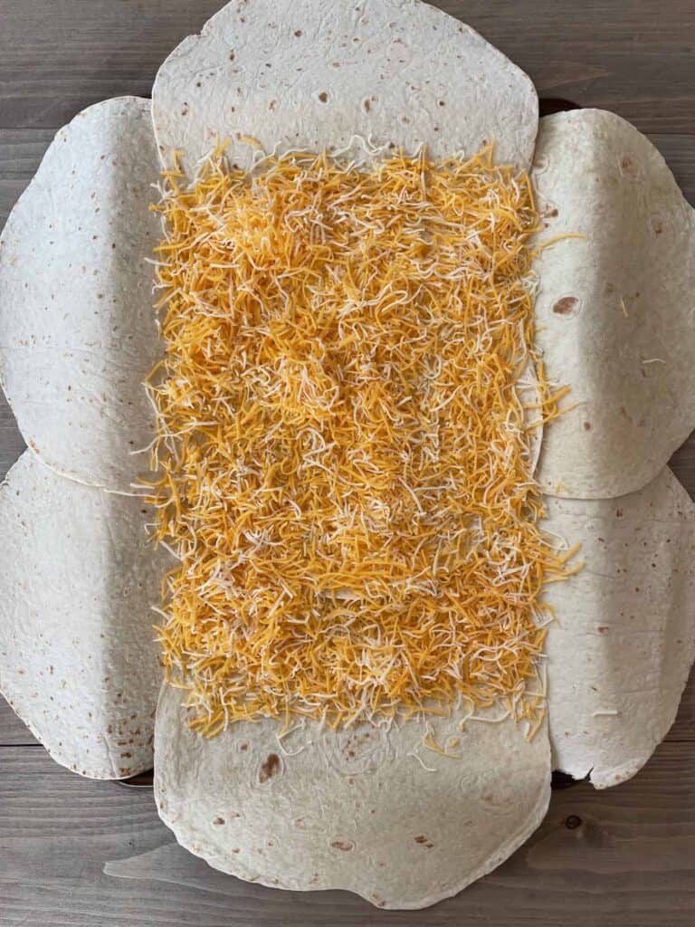 Shredded cheese filling the center of the tortillas on the sheet pan.