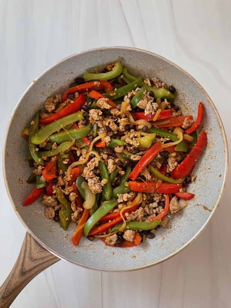 Sautéed peppers, onions, ground turkey and black beans with fajita seasoning in a sauté pan.