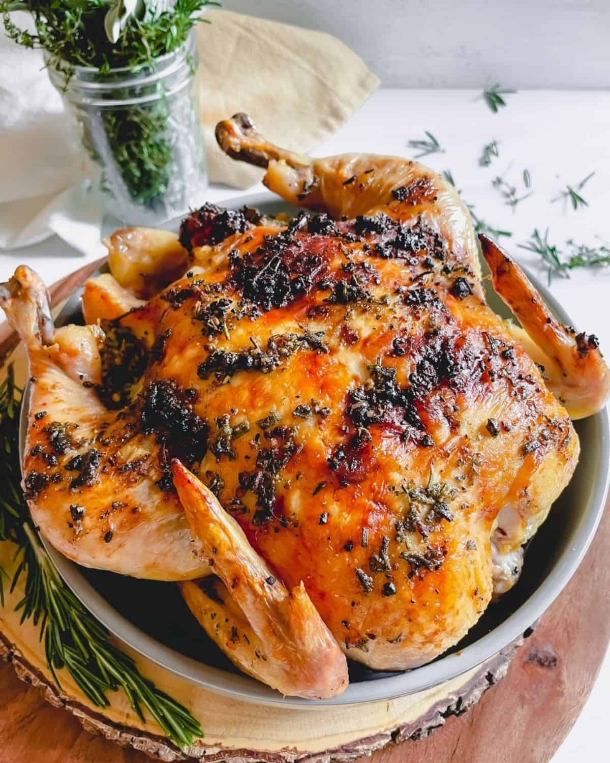 Roasted Chicken with Garlic Herb Butter displayed on a round wooden tray surrounded with fresh herbs