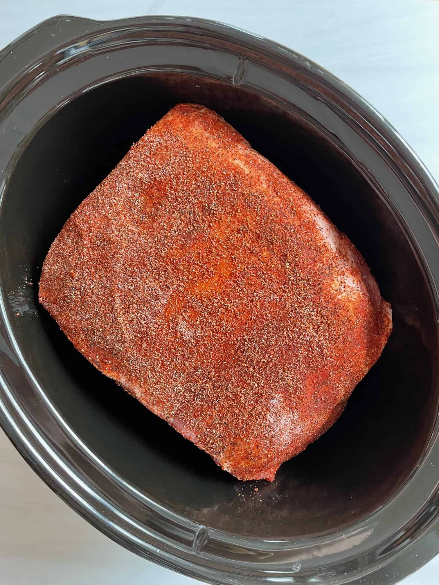 Pork butt is in a black slow cooker