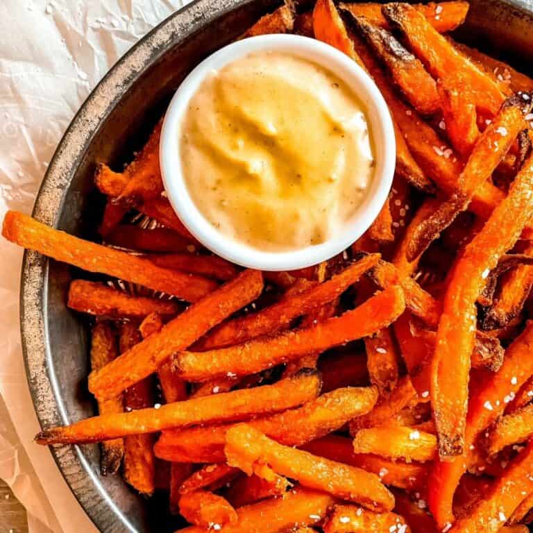 zoomed in image of air fryer sweet potato fries in a round metal tin with honey mustard sauce on the side