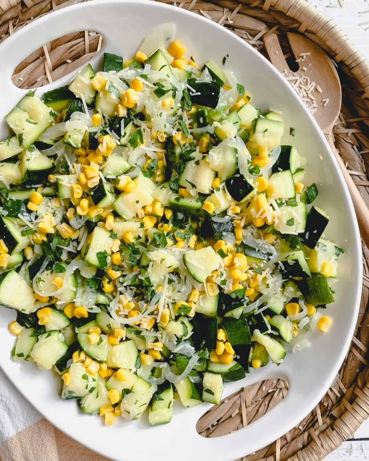 sautéed zucchini and onions with sweet corn in a round white serving bowl on  a basket with a large wooden spoon