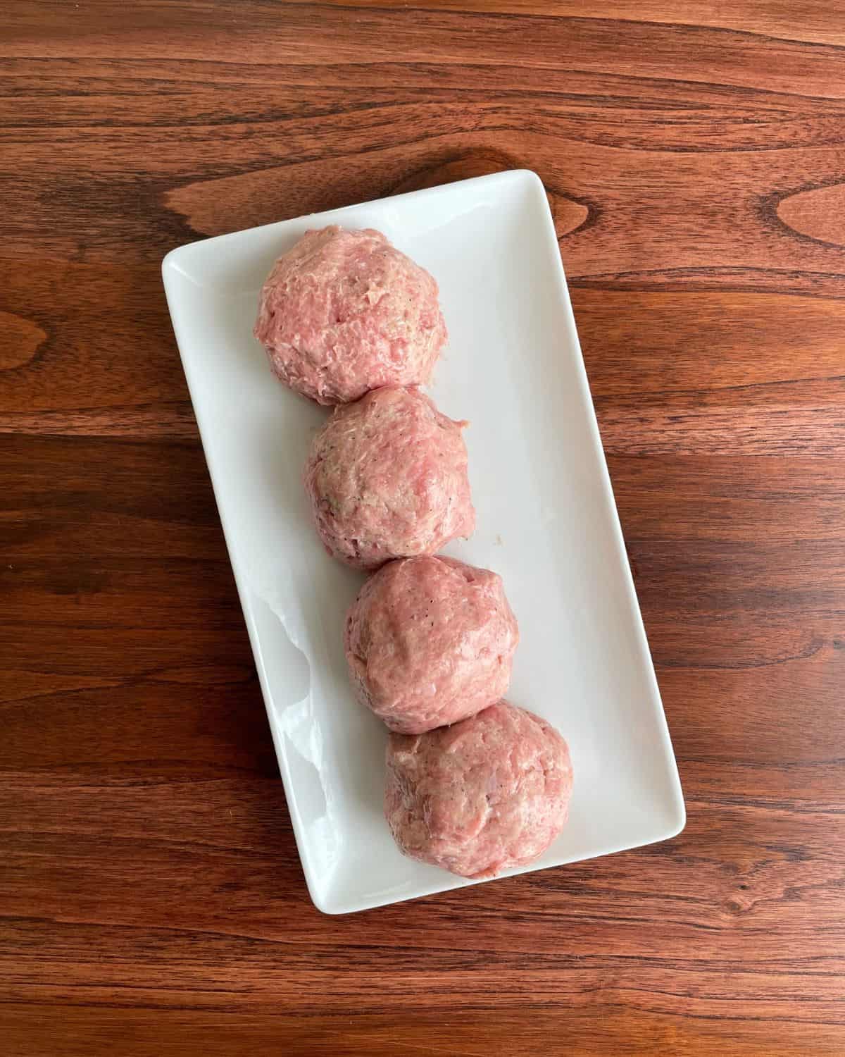 Ground turkey mixed with seasonings rolled into four equally sized balls, on a white plate.