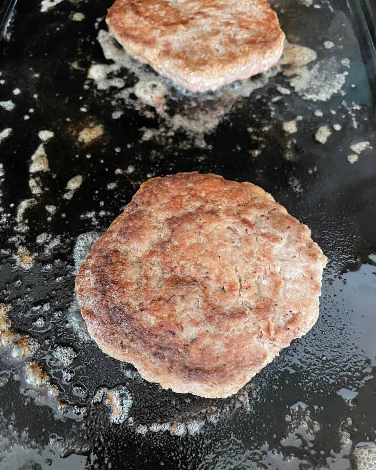 Two smashed turkey burgers cooking on a grill pan.