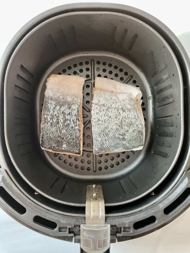 Two pieces of frozen salmon in an air fryer basket, skin side up.