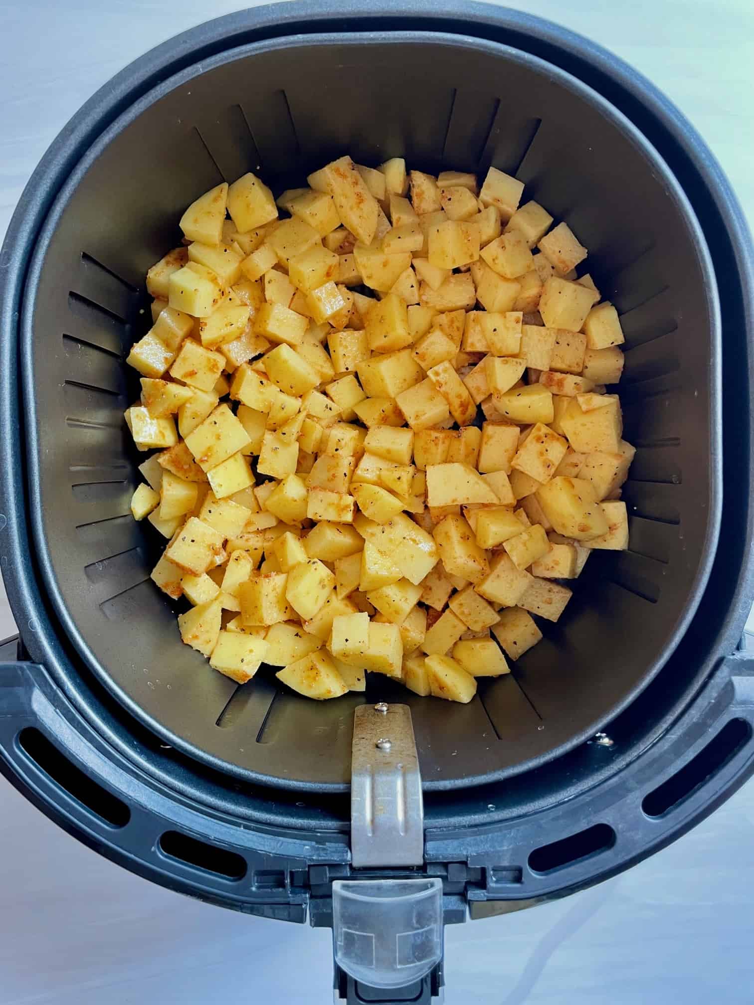 Chopped potatoes in the bottom of an air fryer basket.