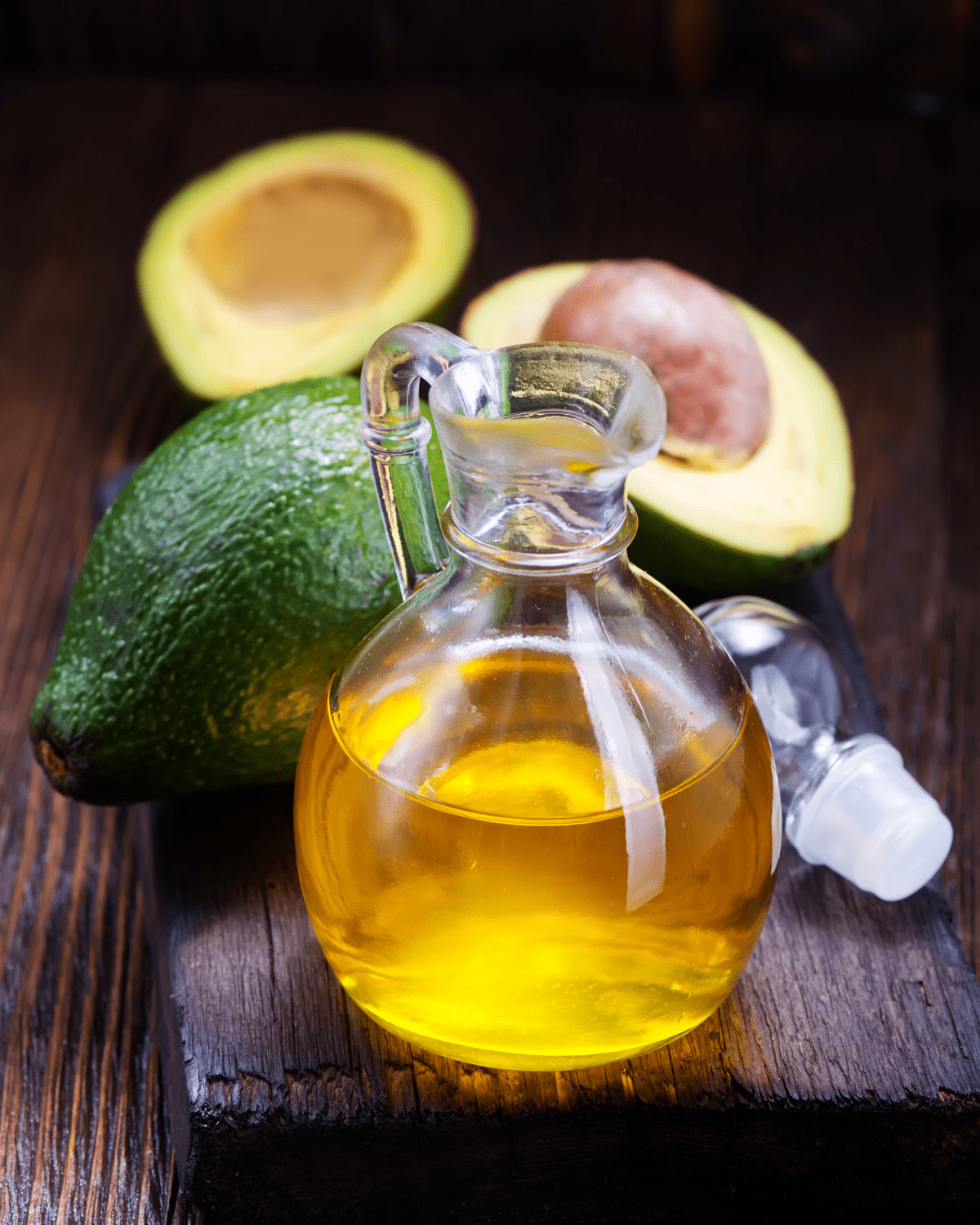 Small glass jar of avocado oil with 2 avocados in the background.
