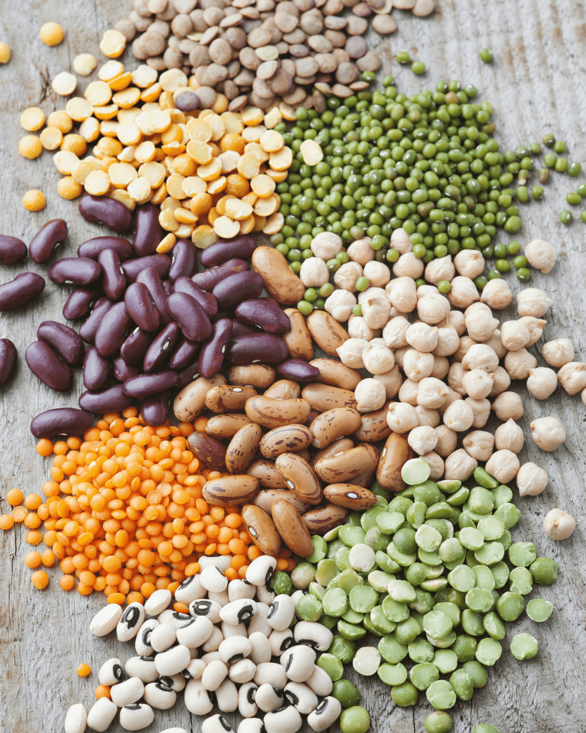A mixture of several different kinds of dried beans on a wooden surface.