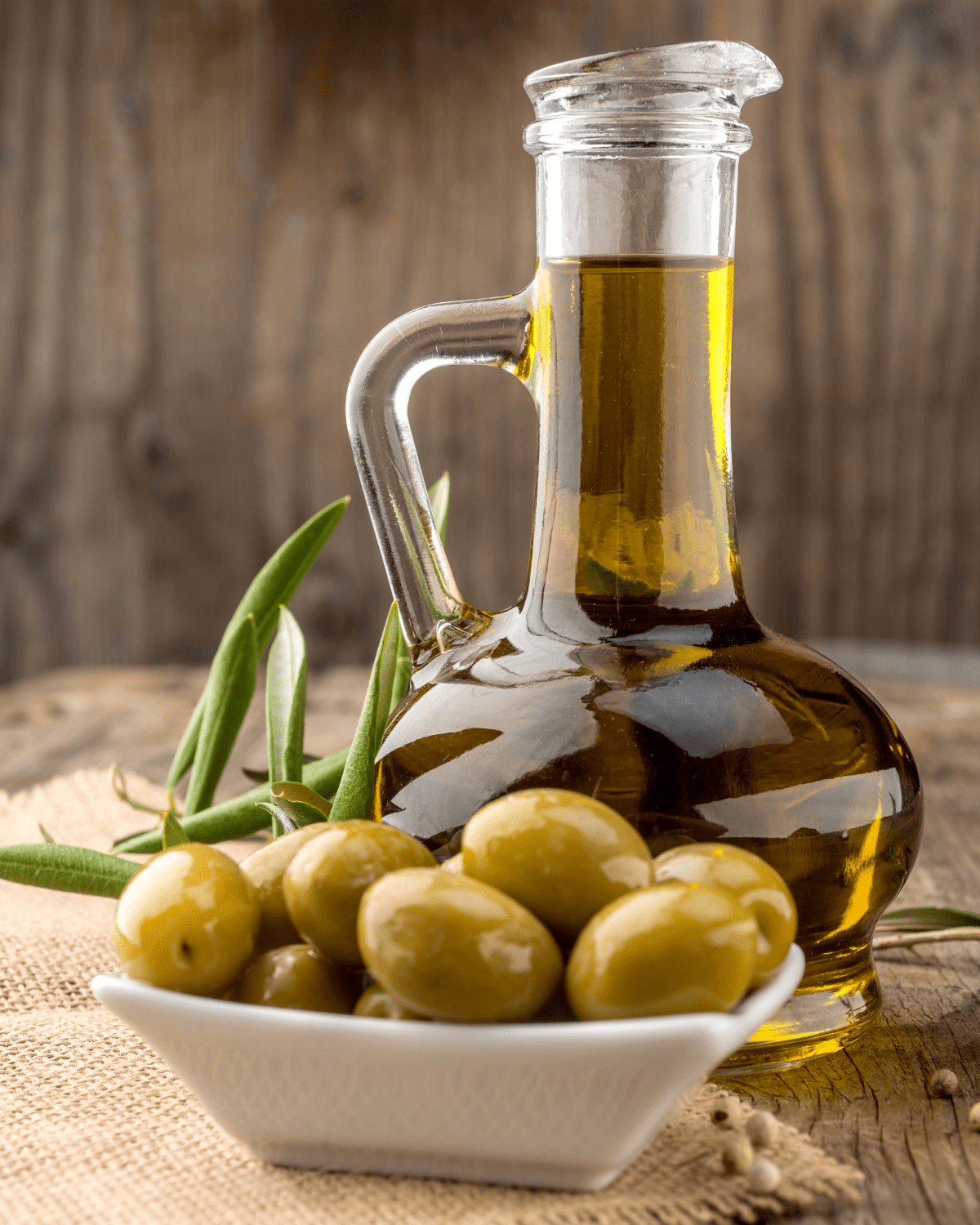 Glass bottle of olive oil behind a small bowl of green olives.