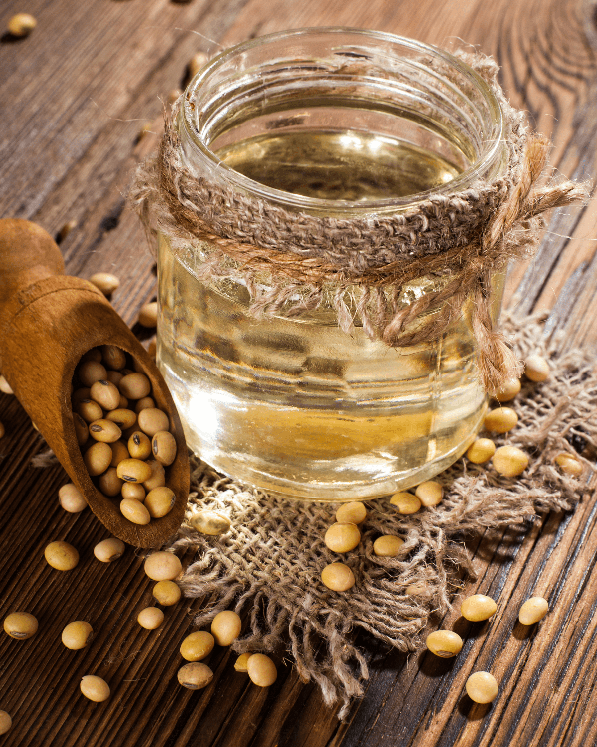 Small glass jar of soybean oil, with dried soybeans around the bottle and a wooden spoon.