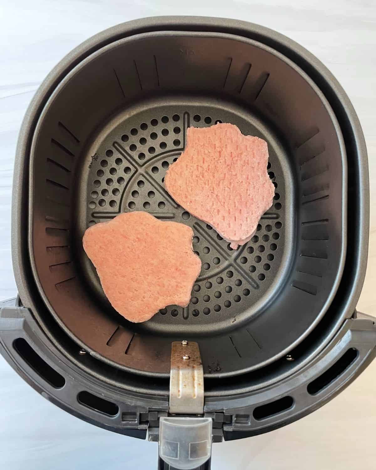 Frozen turkey burgers in the air fryer basket.