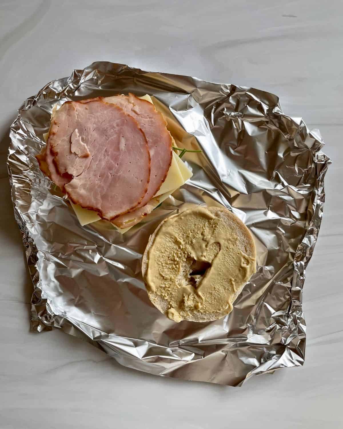 Open bagel on foil with ham, cheese, spinach and Dijon mayo.