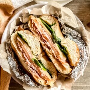 Ham and cheese bagel sandwich with spinach wrapped in foil and parchment paper in a bowl.