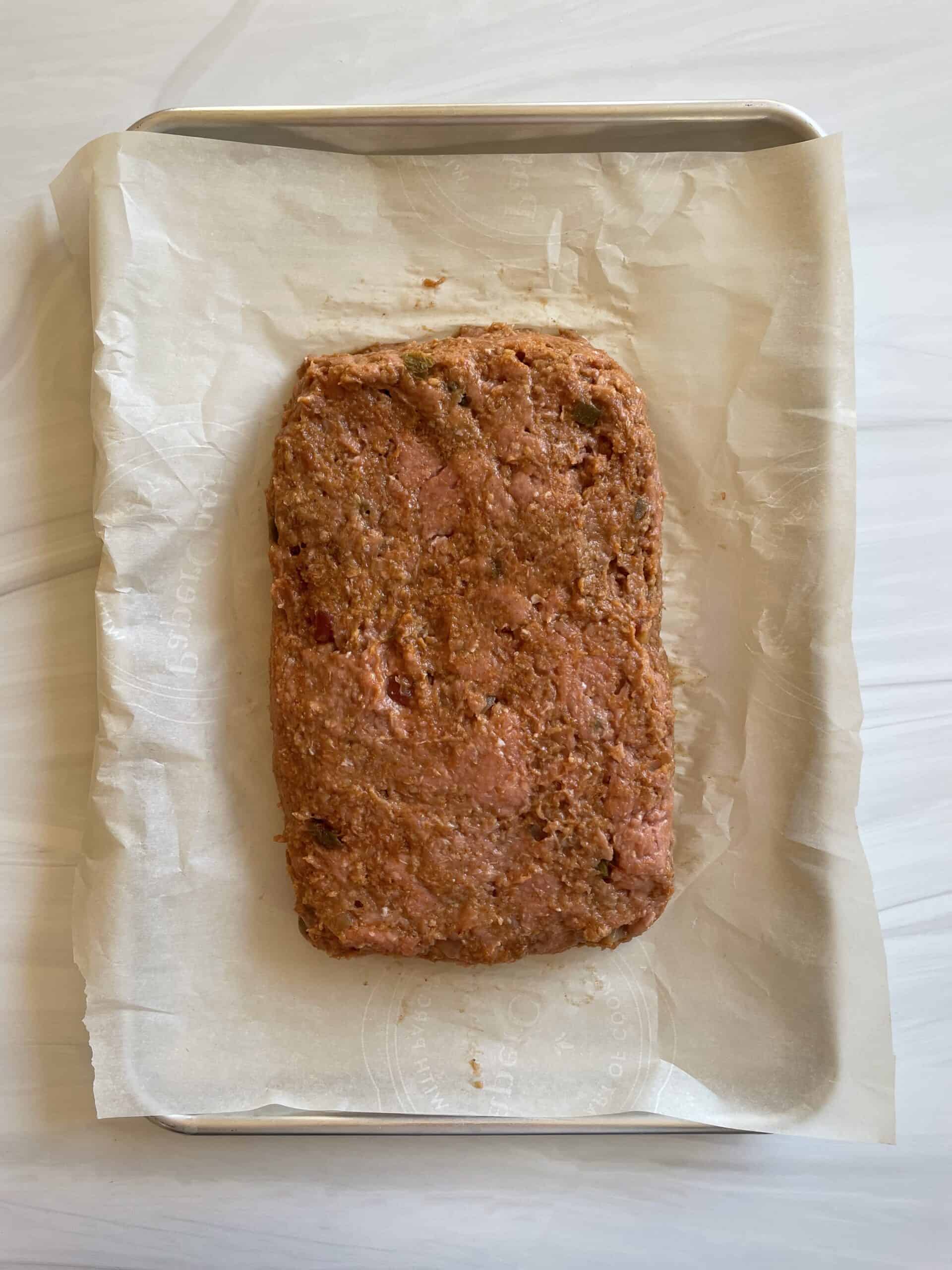 Mexican meatloaf formed in a loaf on a parchment lined sheet pan.