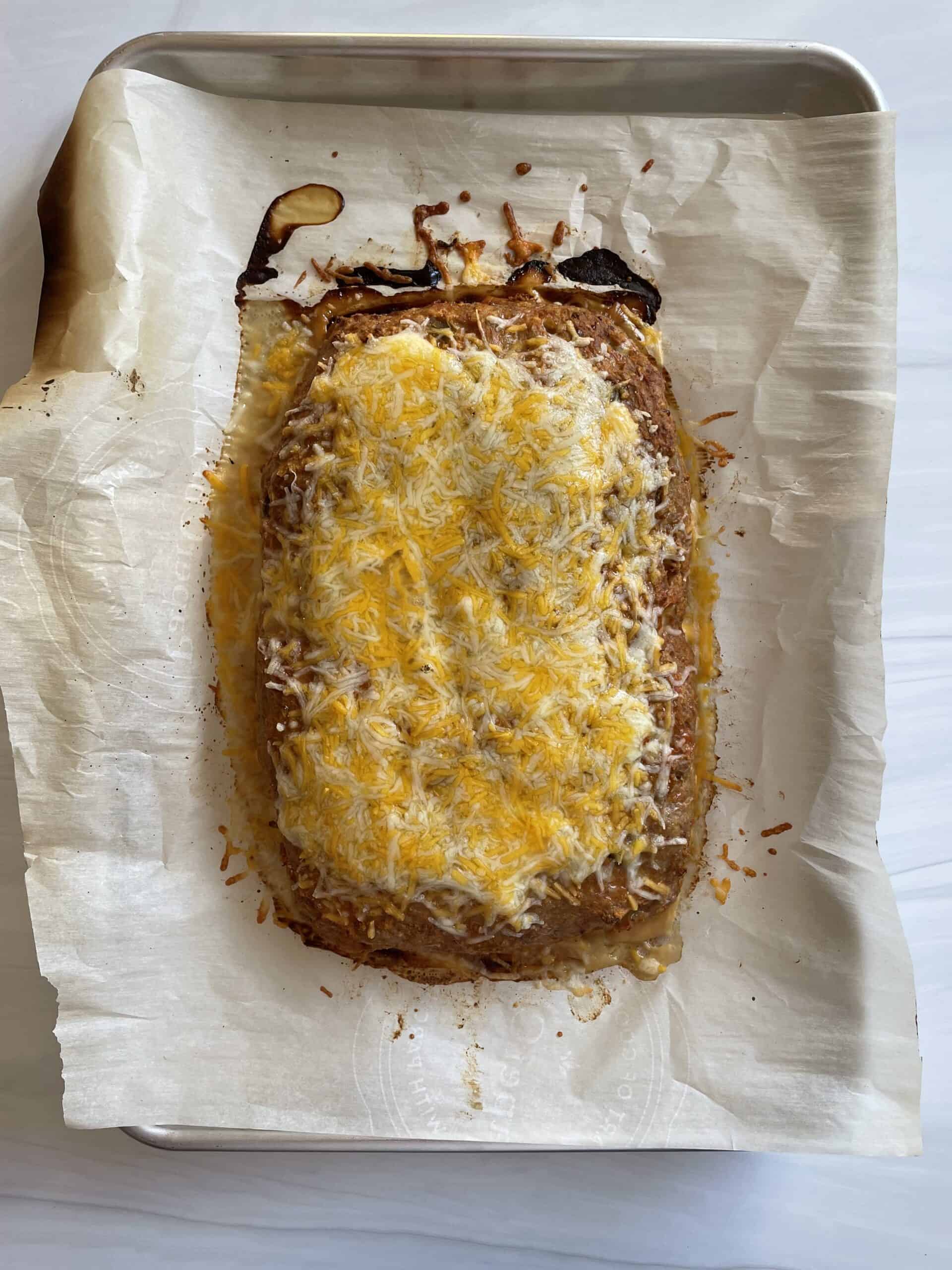 Cooked taco meatloaf on parchment lined baking sheet topped with melted Mexican blend shredded cheese.