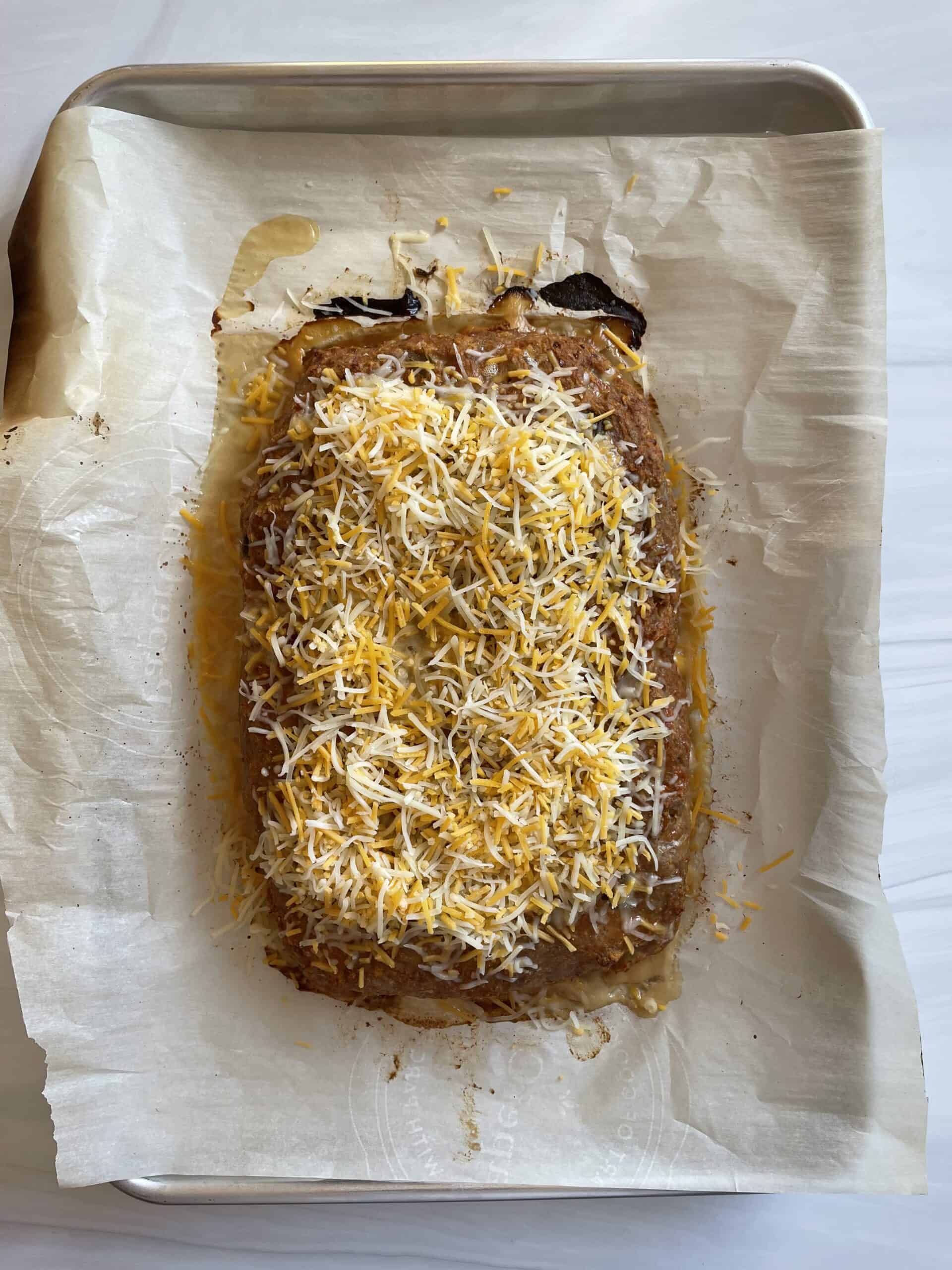 Cooked taco meatloaf on a parchment lined baking sheet topped with cold shredded cheese.