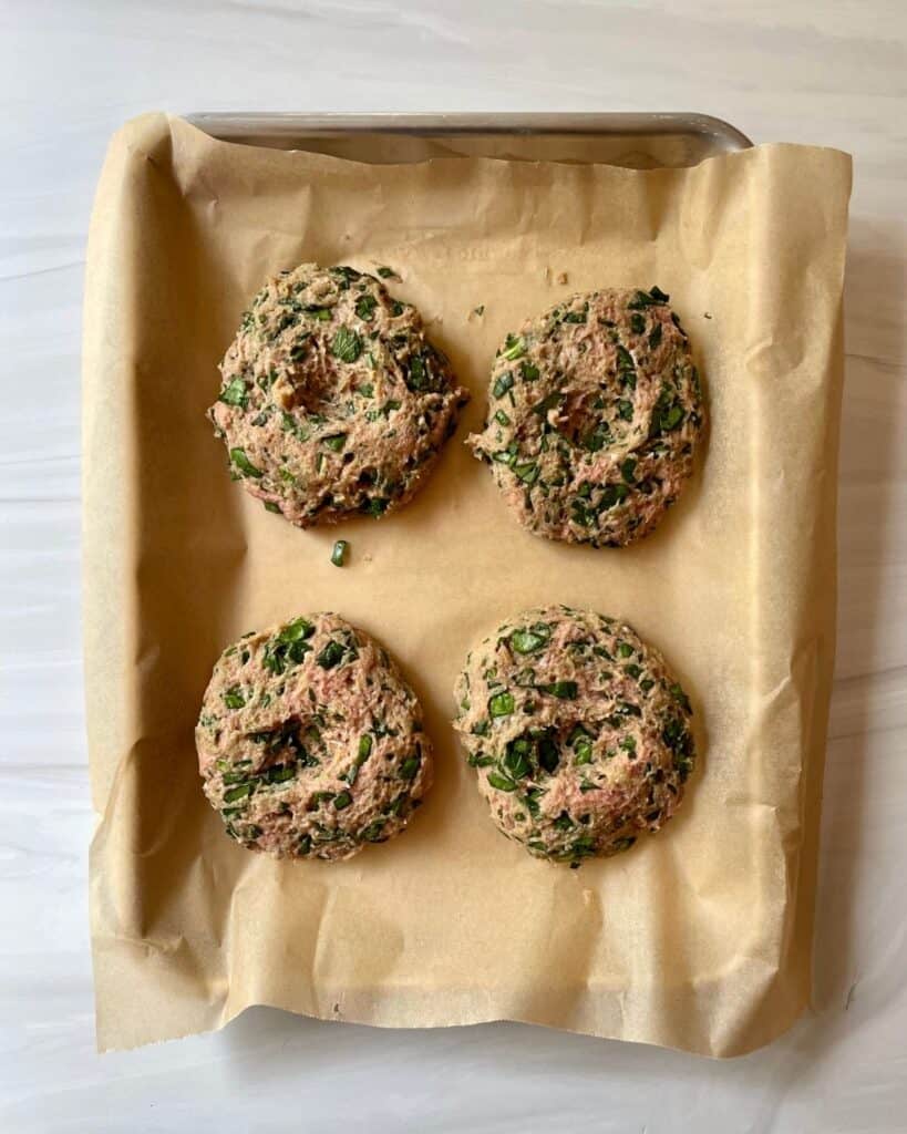 Raw burger patties on a parchment lined baking sheet.