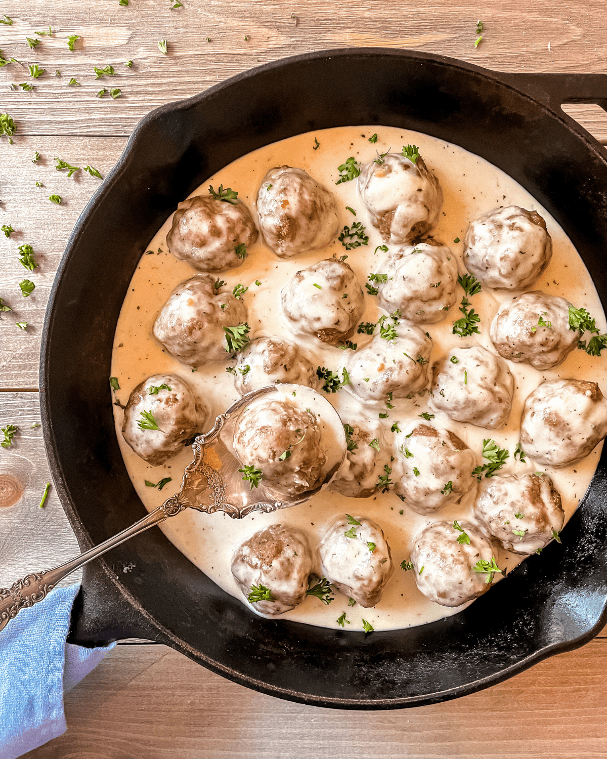 Turkey pesto meatballs in a cast iron skillet, topped with pesto alfredo sauce, garnished with fresh parsley.