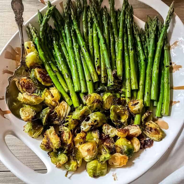 Asparagus and brussel sprouts recipe in a white round serving bowl, with a silver spoon, drizzled with balsamic vinegar glaze.
