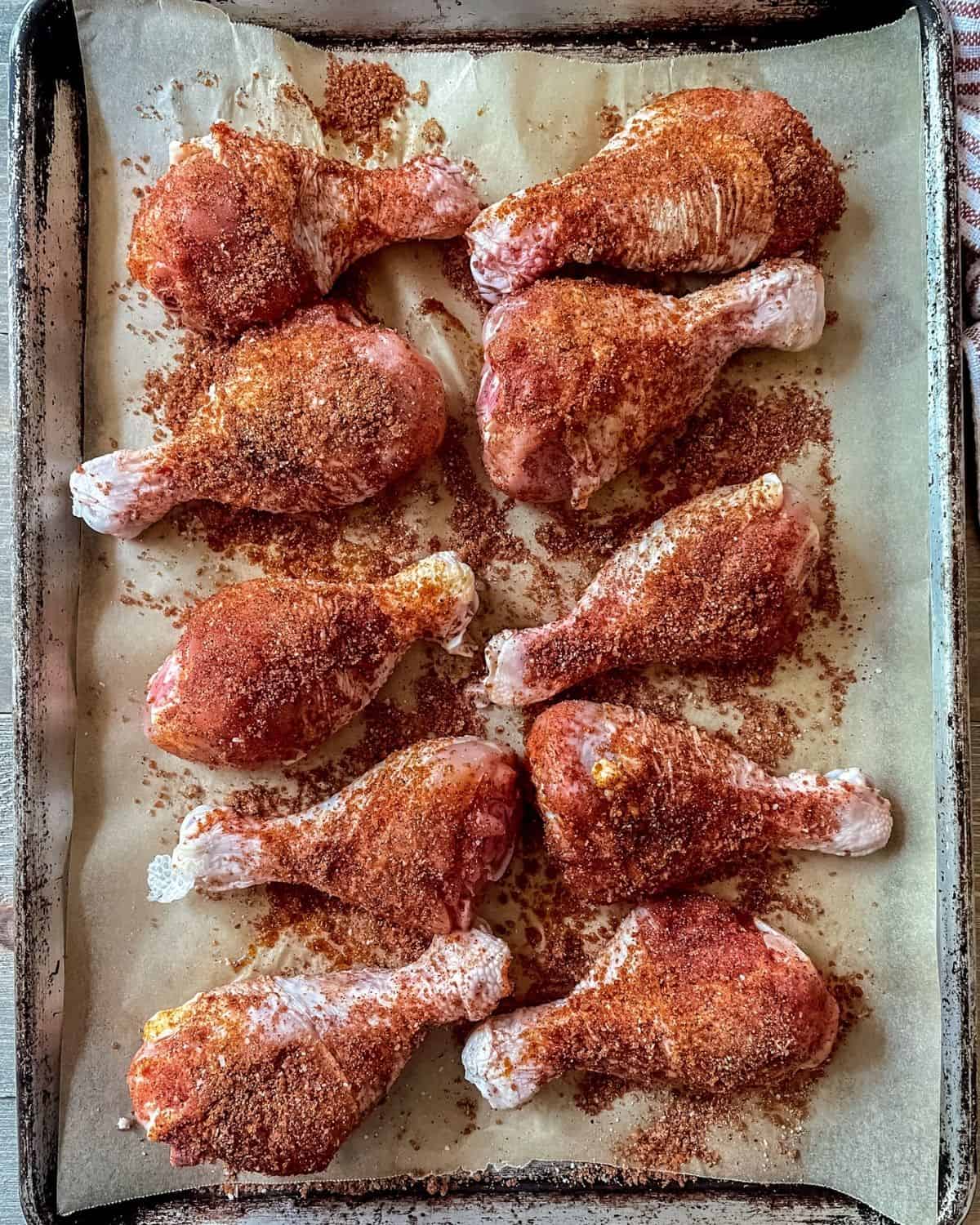 Uncooked chicken drumsticks coated in dry bbq seasoning on a sheet pan.