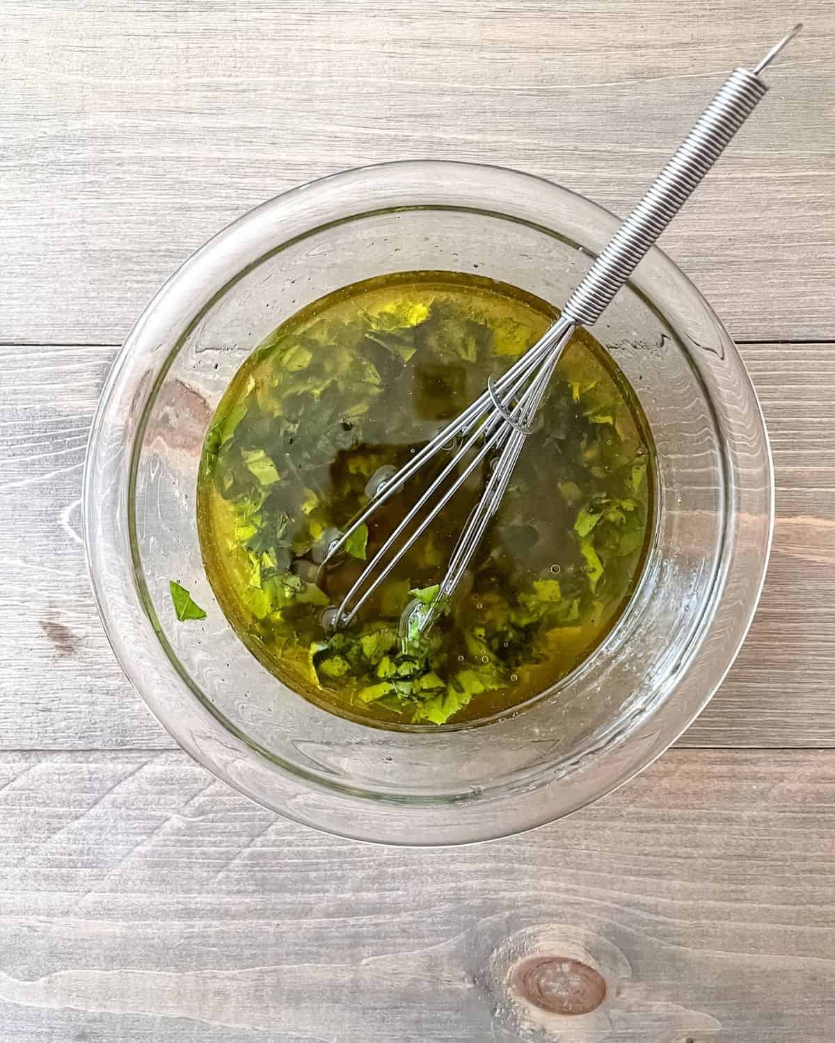 Clear glass bowl of the vegetable marinade and a whisk.