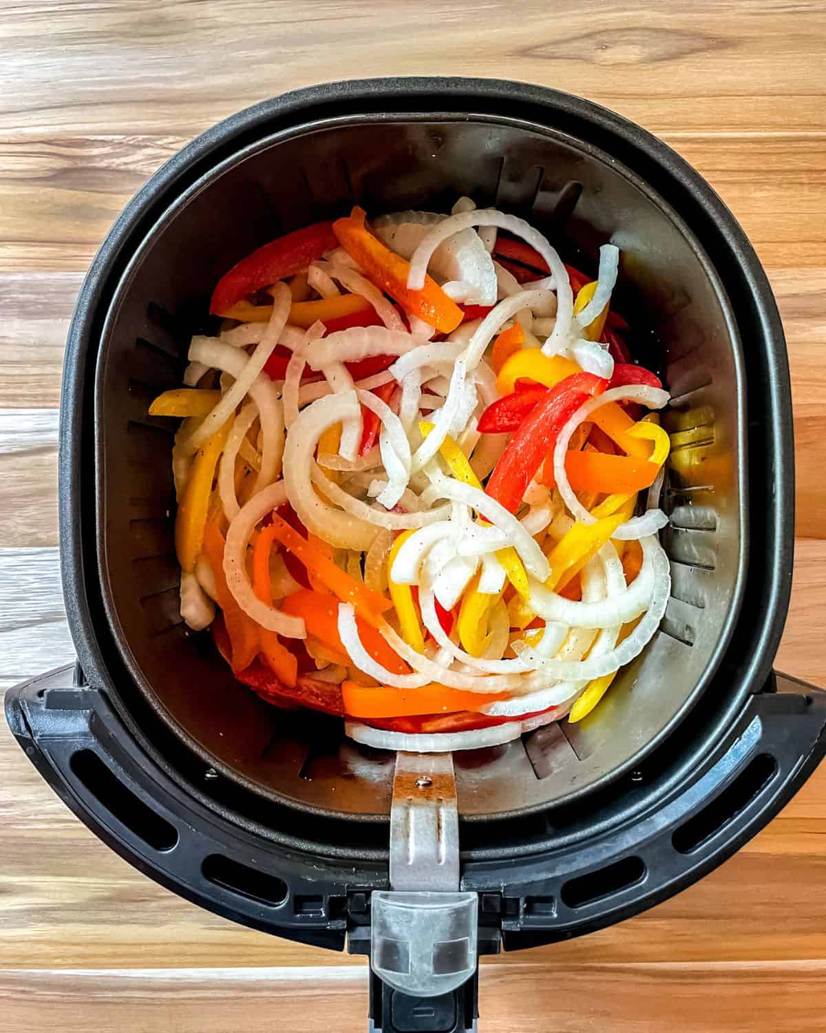Sliced peppers and onions in the air fryer basket.