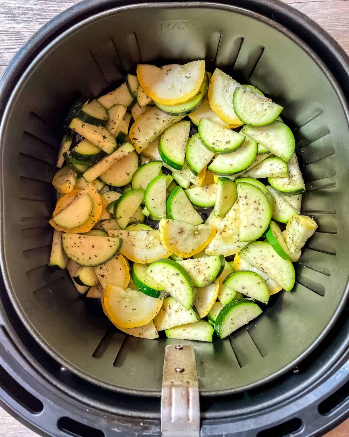 Uncooked zucchini and squash in the bottom of an air fryer basket.