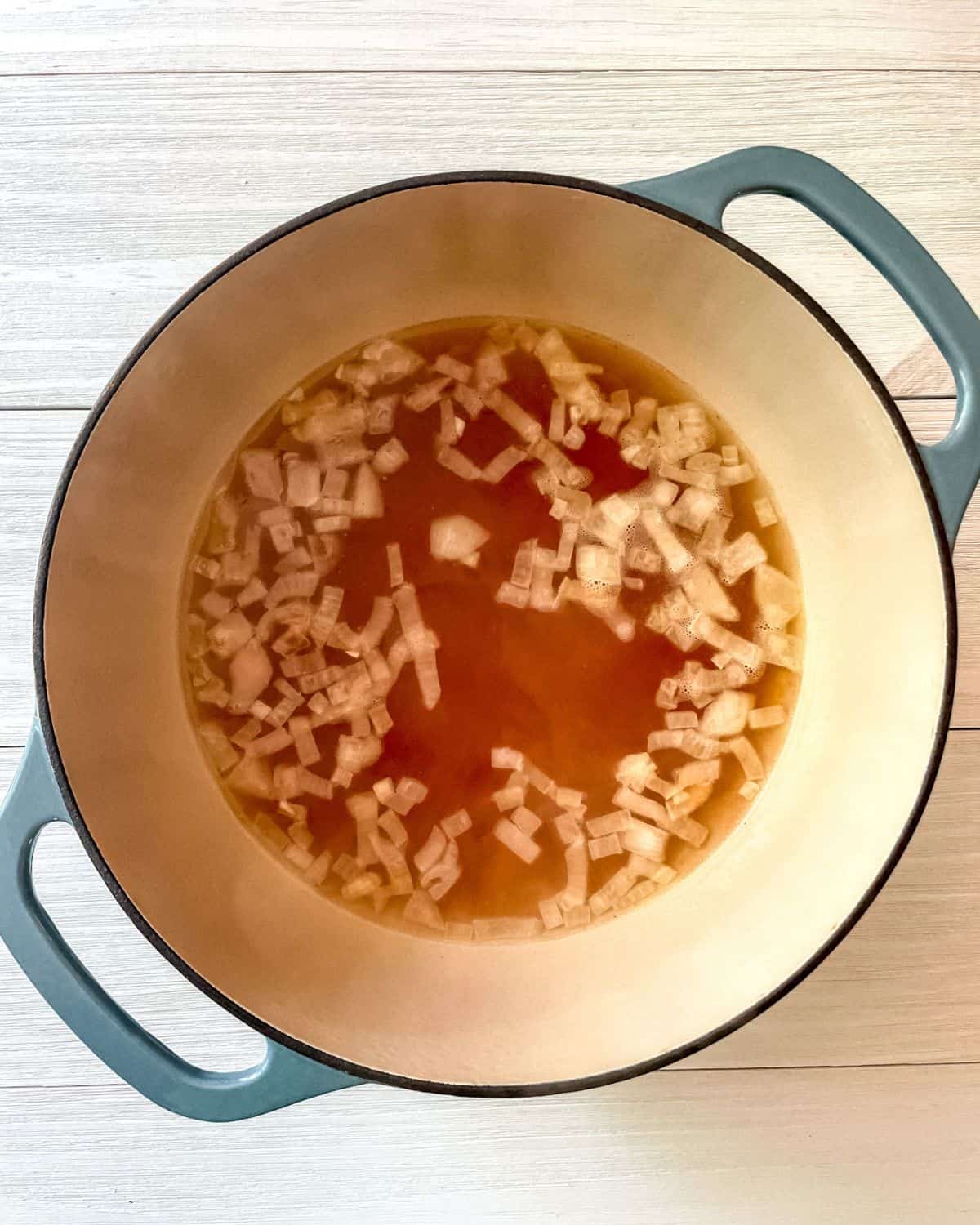 Diced onions and vegetable broth in a blue Dutch oven.