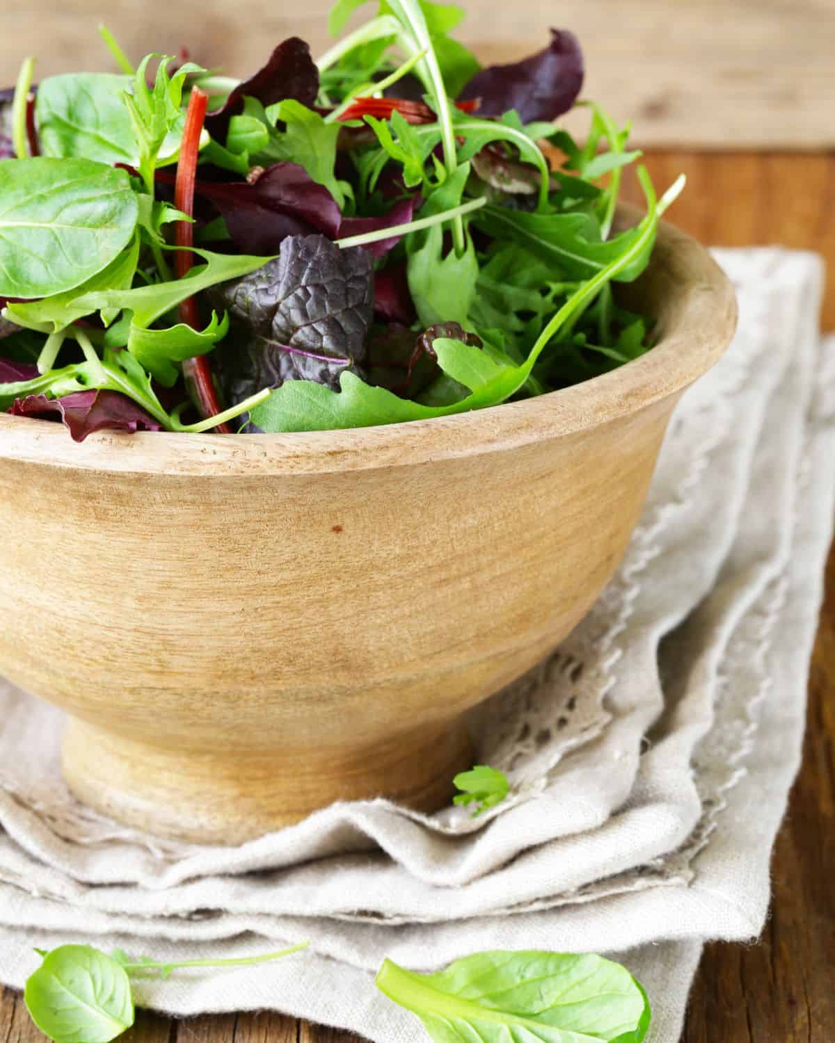 Wooden bowl of mixed greens on a cloth napkin.