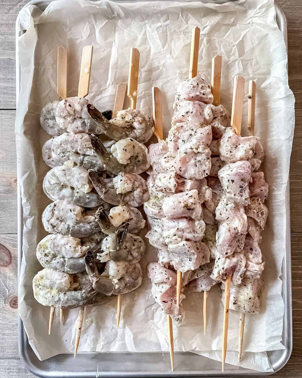 Raw shrimp and chicken kabobs on a parchment lined baking sheet.