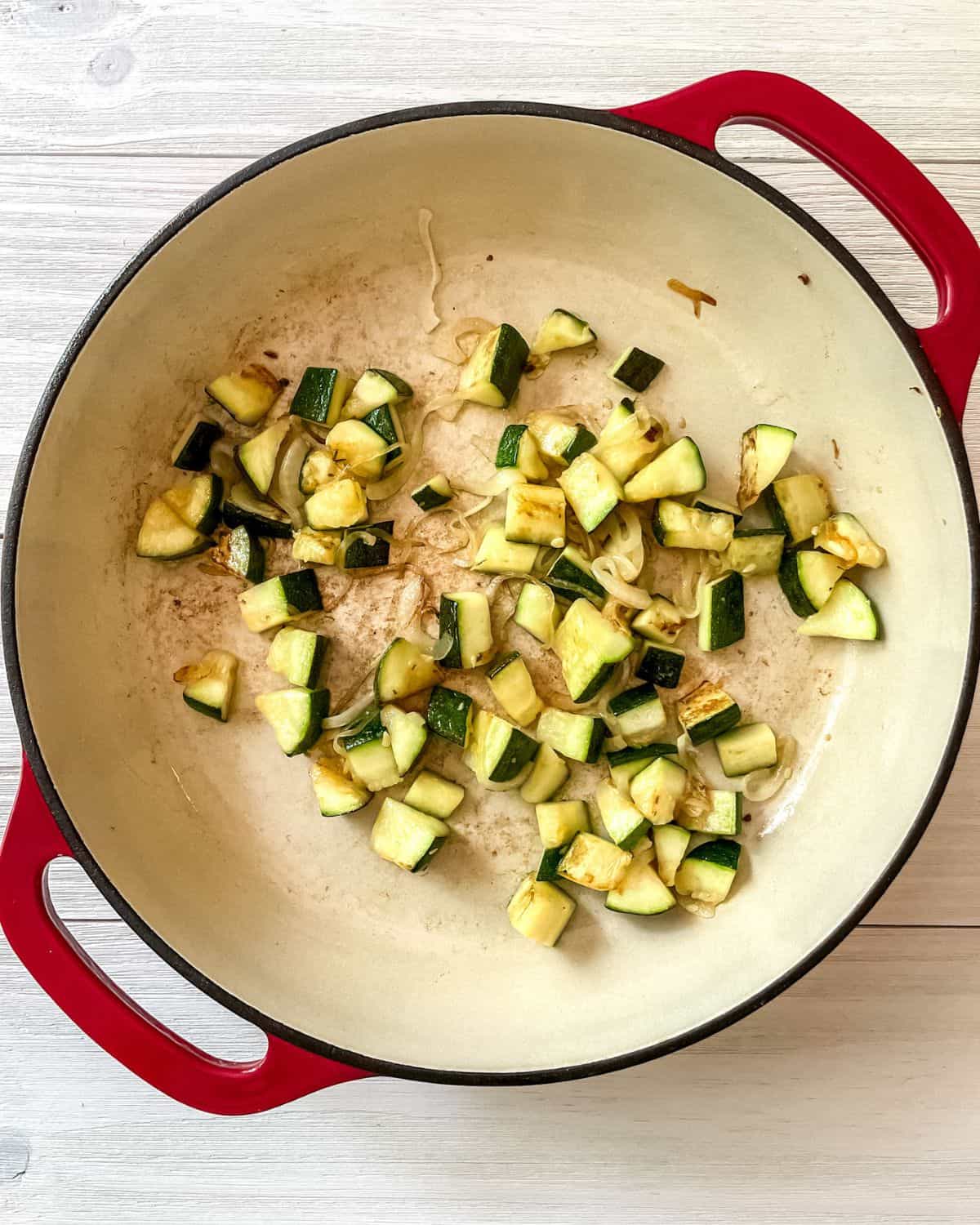 Sautéed zucchini and onion in a red skillet.