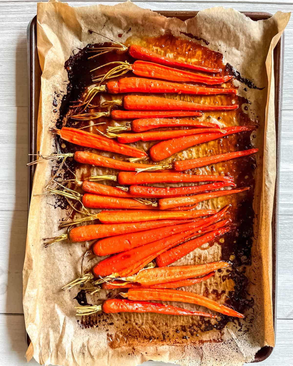 Roasted brown sugar glazed carrots on a parchment lined baking sheet.
