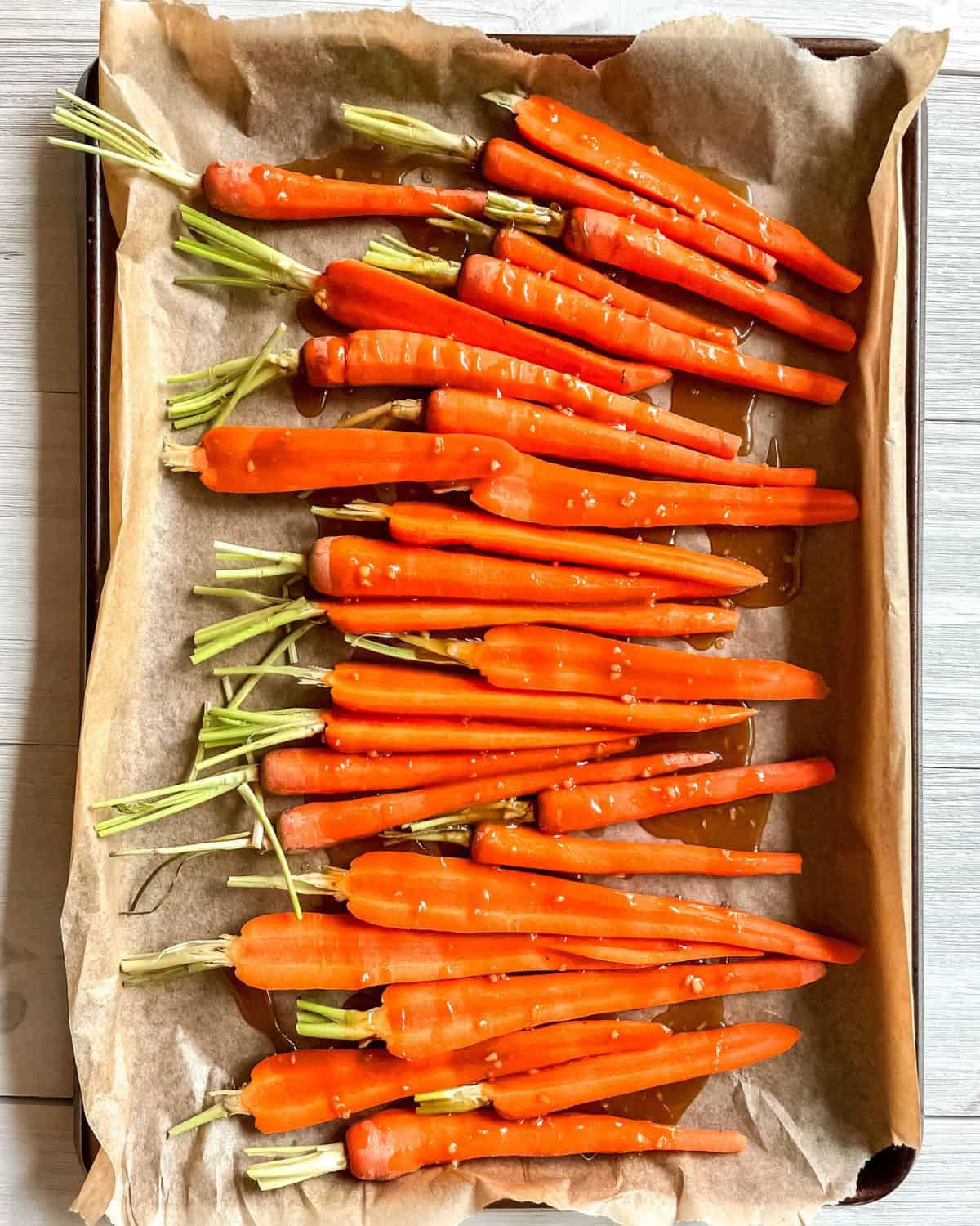 Carrots on a parchment lined baking sheet, drizzled with brown sugar glaze