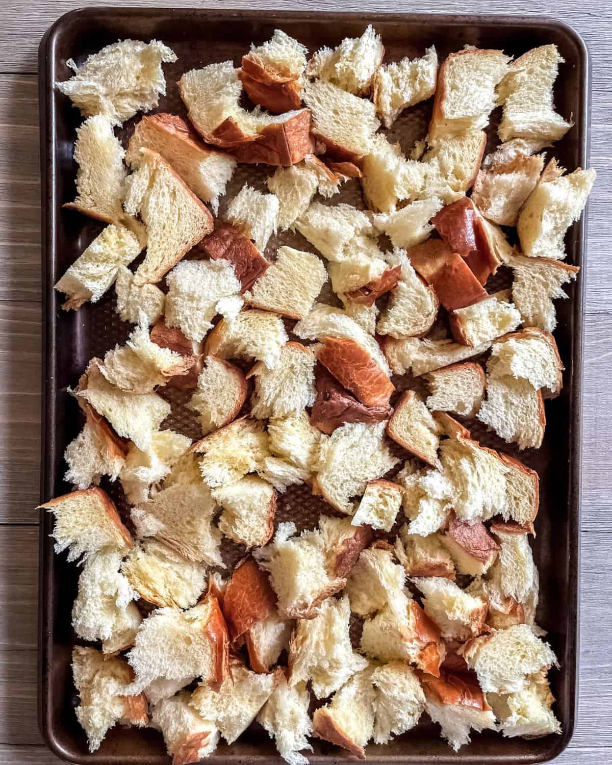 Ripped pieces of fresh brioche bread on a sheet pan.