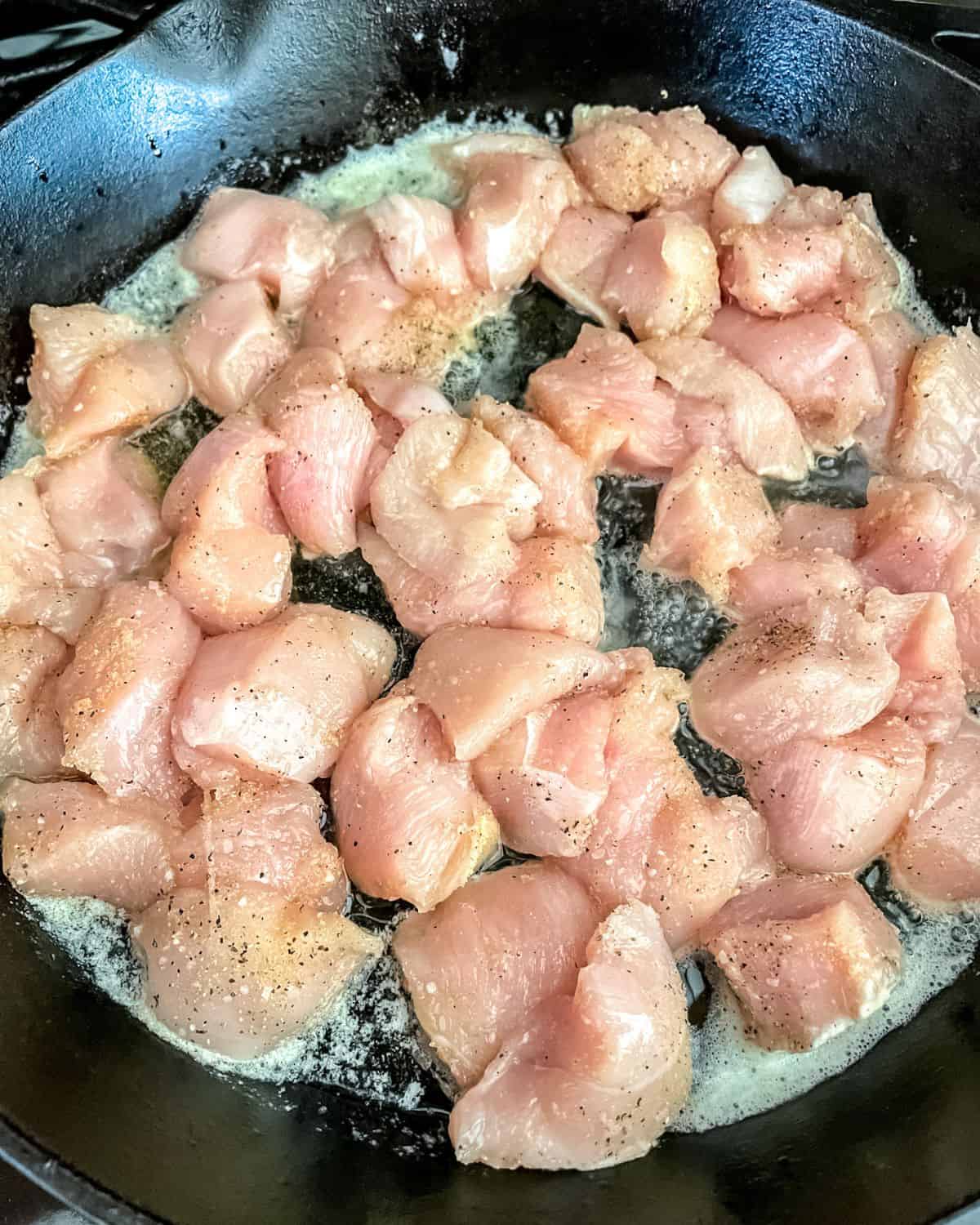 Raw chicken cooking in a cast iron skillet.
